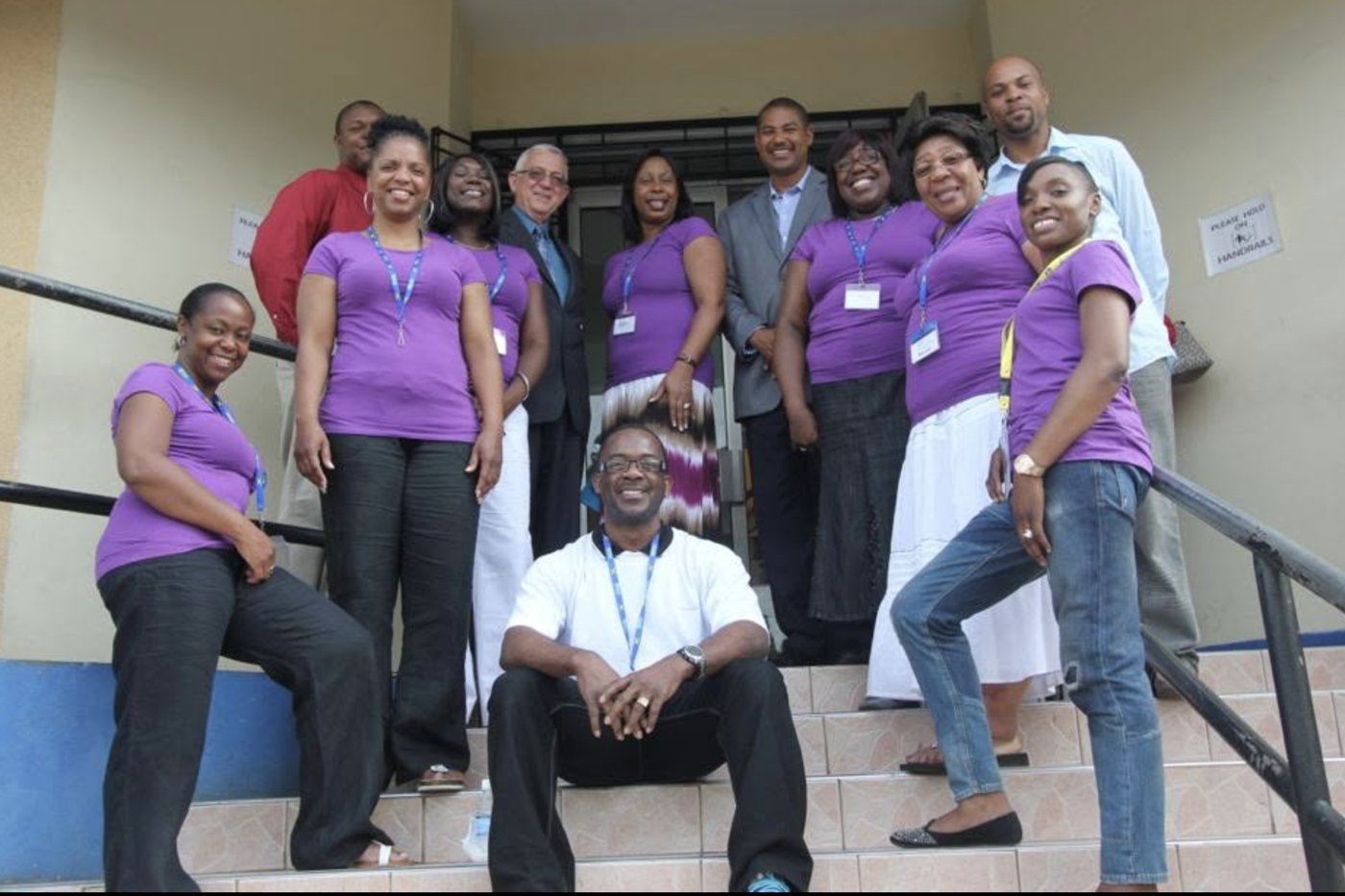 A group of Jarrett Foundation volunteers in purple T-shirts, smiling on the front steps of a school